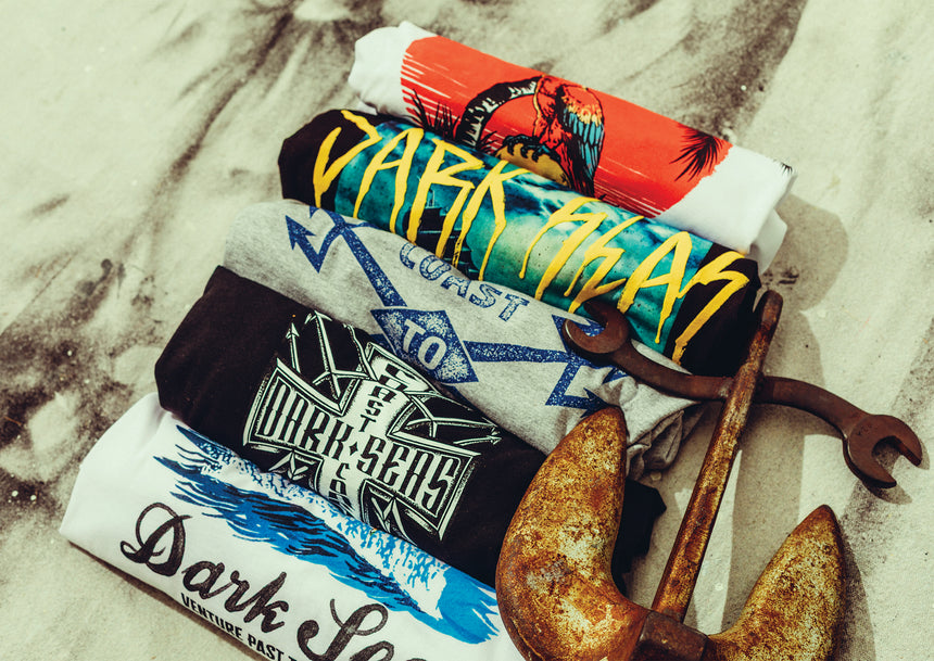 Five Tee shirt rolled in bundles with a rusty anchor beside them and a canvas background.